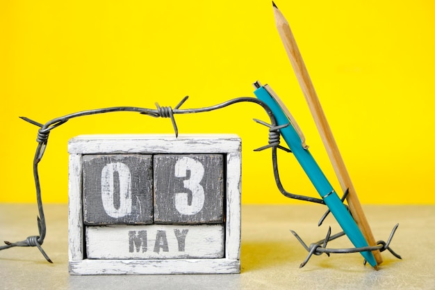 May 3 on calendar barbed wire ballpoint pen and pencil yellow backgroundconcept for press freedom day