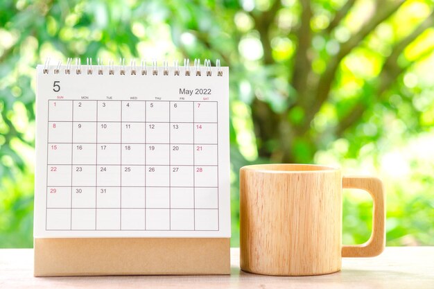 Mese di maggio, scrivania del calendario 2022 per l'organizzatore alla pianificazione e tazza di caffè in legno su tavola di legno con sfondo verde natura.