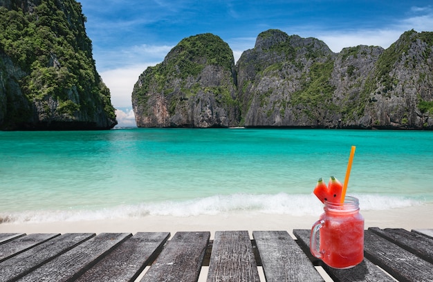 Maya bay island view with wooden board and cold drink glass in sun lighting.