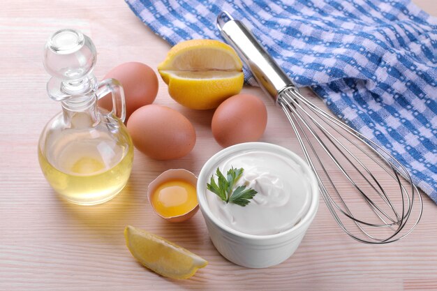 Mayonnaise in a white ceramic bowl and ingredients for making mayonnaise on a natural wooden background. white sauce.