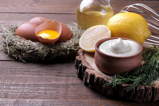 Mayonnaise in a wooden bowl and ingredients for making mayonnaise on a brown wooden background white sauce