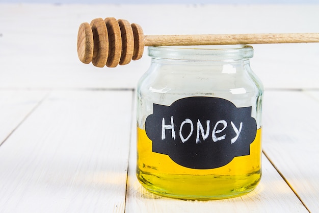 Foto mead jar gelabeld met honing met een druppelaar, op een witte tafel.