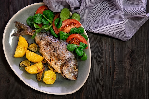 Meal.Baked Dorado fish with vegetables in the oven on a dark background.