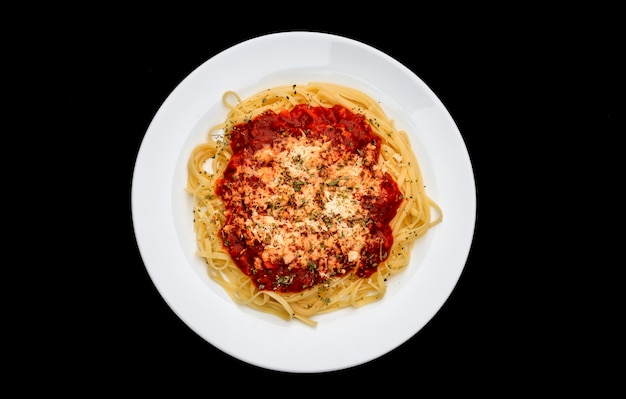 Meal of noodles with red sauce and grated cheese on white plate, black background, top view