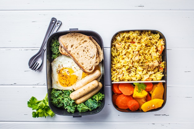 Meal prep containers with rice with chicken, baked vegetables, eggs, sausages and salad overhead shot.