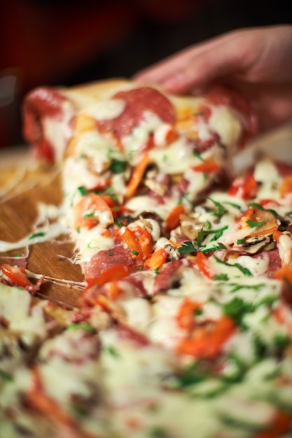 ピザの食事時間、非常に薄い被写界深度で撮影されたピザのスライスを取る人。フレーム。手はピザのスライスをカットし、それを取り、マクロ撮影します。ピザとピザのスライスを手に