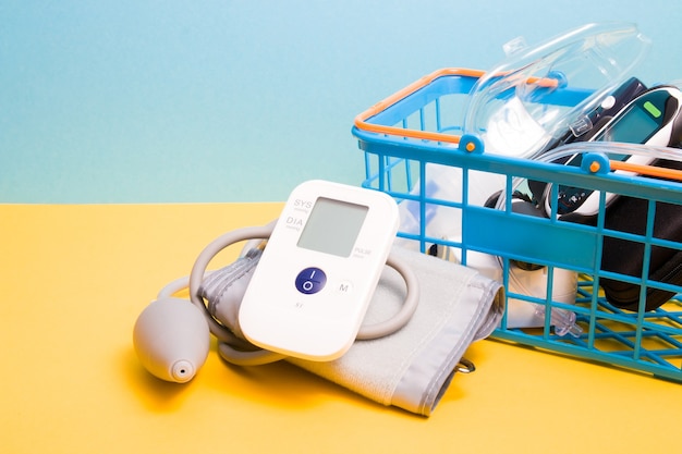 Measure blood pressure monitor lies next to a small blue shopping basket in which there is a glucose meter and a nebulizer for inhalation