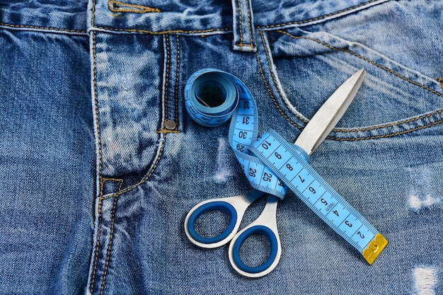 Measure tape around metal scissors on jeans fabric