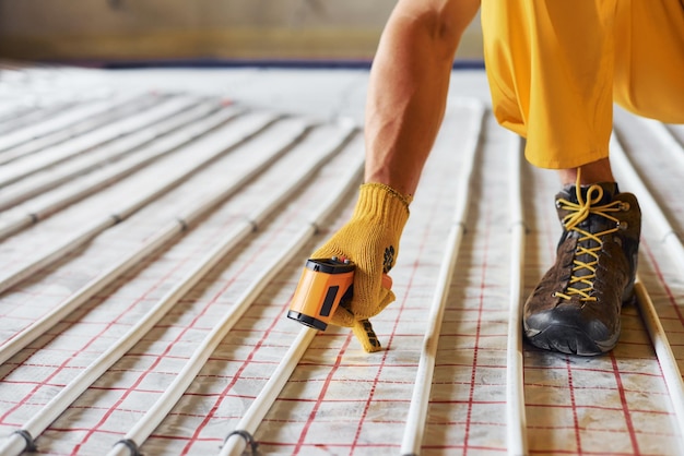 Photo measures heat of the pipes worker in yellow colored uniform installing underfloor heating system