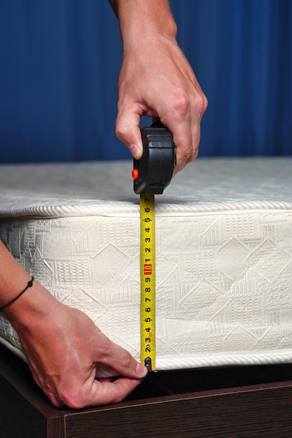Измерение высоты матраса сантиметровой лентой. Удобная для сна ортопедическая кровать. Фото высокого качества