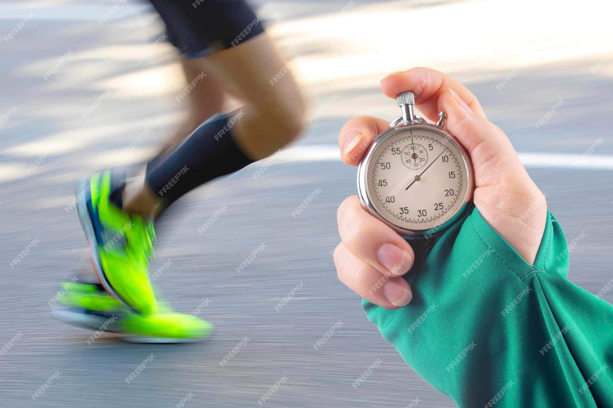 Premium Photo  Measuring the running speed of an athlete using a  mechanical stopwatch hand with a stopwatch on the background of the legs of  a runner feet running