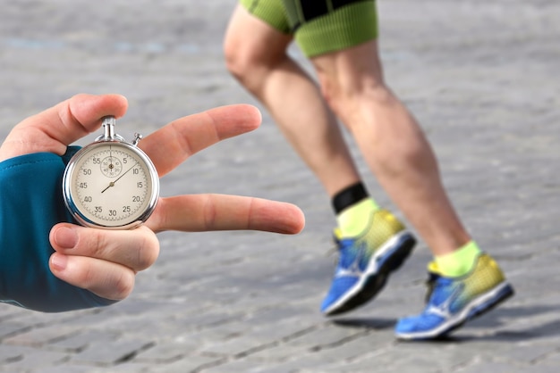 Measuring the running speed of an athlete using a mechanical stopwatch hand with a stopwatch on the background of the legs of a runner