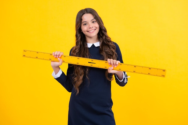 学校の設備を測定する黄色の背景に分離された幾何学の授業のための測定を保持している女子高生学生の研究数学