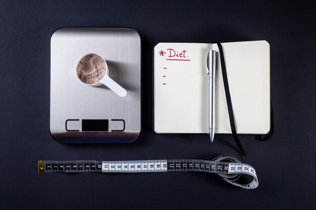 Measuring scoop of whey protein, notebook, weight scale and measuring tape for diet. 