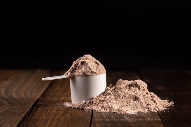 Photo measuring scoop of whey protein on wooden table to prepare a milkshake.