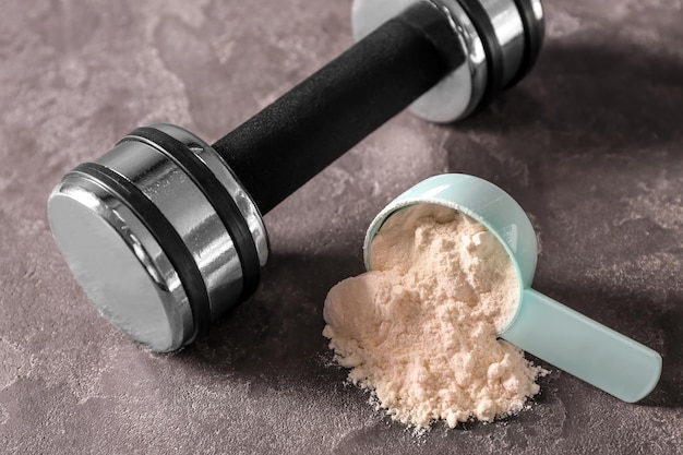 Measuring scoop with protein powder and dumbbell on grey background