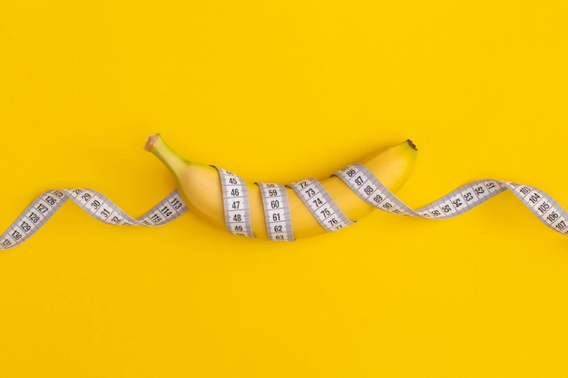 measuring tape and banana on yellow background. weight loss concept
