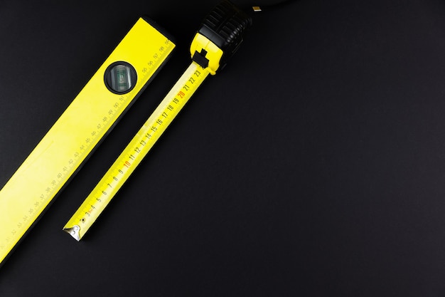 Measuring tape and construction level in yellow on a black background