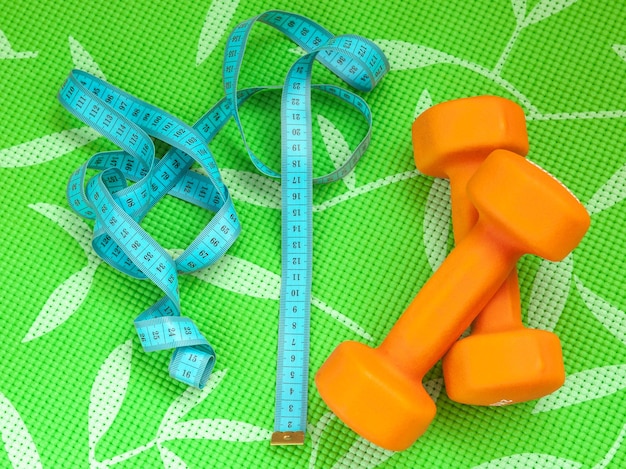 Measuring tape for controlling body volume and orange dumbbells for fitness on a green background