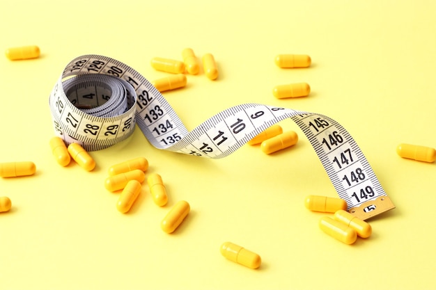 Measuring tape and diet pills on a colored background closeup