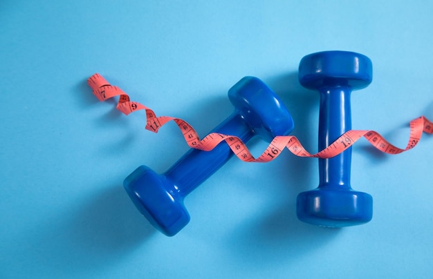 Measuring tape and dumbbells on the blue background