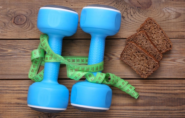 Measuring tape and dumbbells diet whole grain rye bread on wooden background Weight loss diet fitness concept