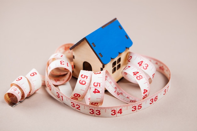 Measuring tape and house on white surface