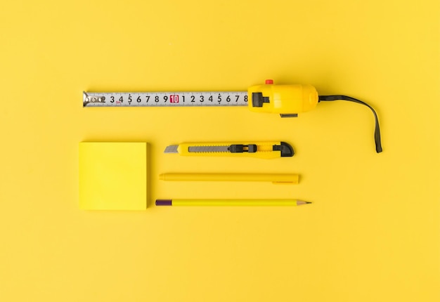 노란색 배경에 테이프 펜 연필 칼과 종이를 측정합니다.