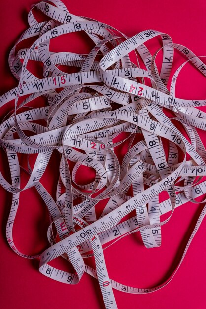 Photo measuring tape rolled out randomly on red background.