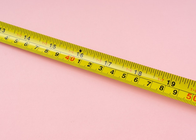 Nastro di misurazione con centimetri e pollici su sfondo rosa.