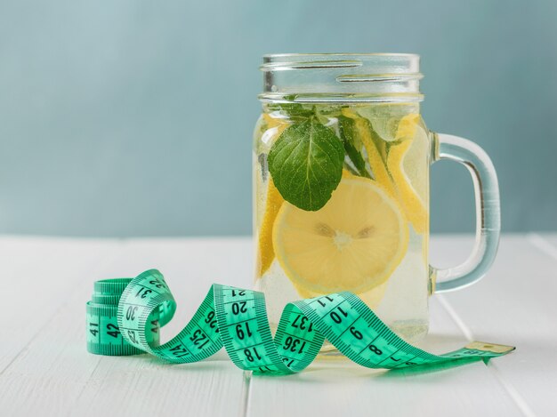 Measuring tape with a mug with a drink of lemon and mint on a white wooden table