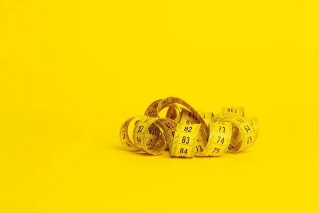 Measuring tape on a yellow background. Measuring tape in the shape of a spiral twisted on a yellow background. Slimming and diet concept, copy space