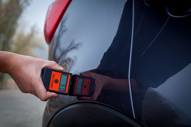 Measuring the thickness of the car paint coating in black color using a paint thickness gauge.