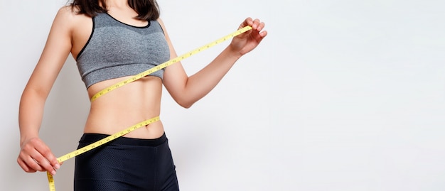 Measuring waist with a tape. Fit and healthy woman on gray isolated