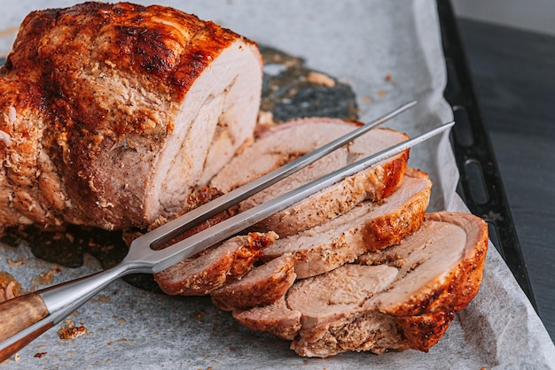 Meat baked on a baking sheet and parchment paper next to a meat fork