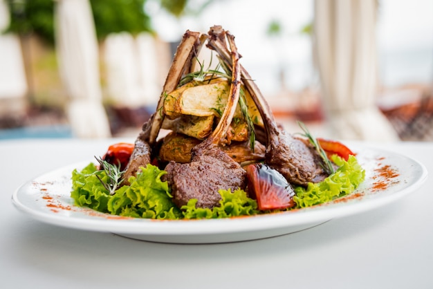 Meat on the bone with vegetables on a white plate.