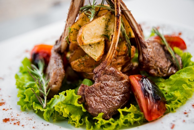 Meat on the bone with vegetables on a white plate.