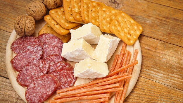 Meat and cheese plate for appetizers sausage cheeses crackers\
nuts on wooden