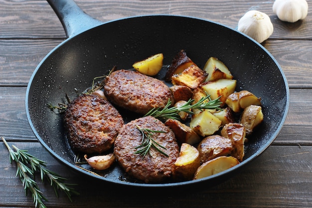 Meat cutlets with fried potatoes and rosemary in a frying pan on a wooden table