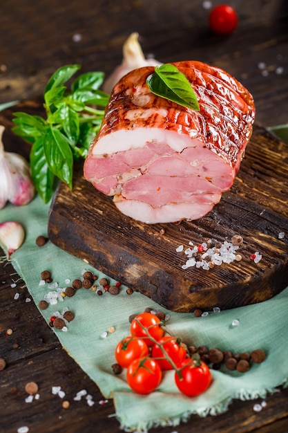 Мясной деликатес, вареная свинина красивая, целая или нарезанная на кухонной разделочной доске, специи