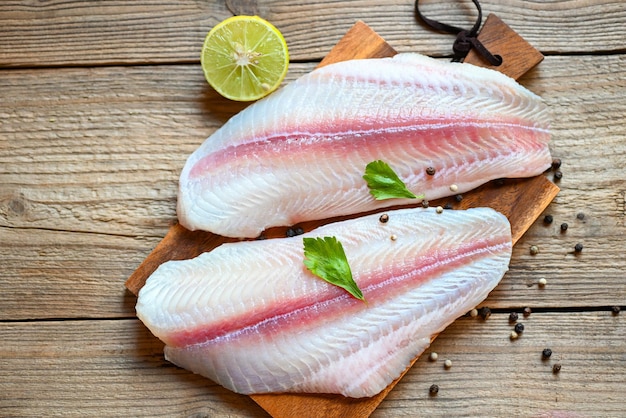 Carne dolly pesce tilapia filetto di pesce gatto striato su tavola di legno con ingredienti per cucinare filetto di pesce pangasio crudo fresco con erbe e spezie pepe nero limone lime