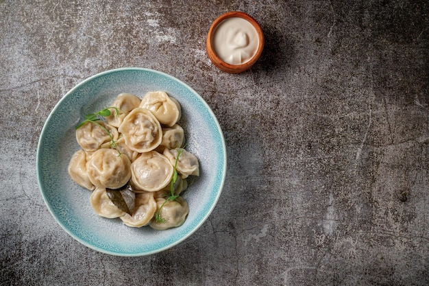 Пельмени со специями на тарелке с зеленью на фоне серого каменного стола