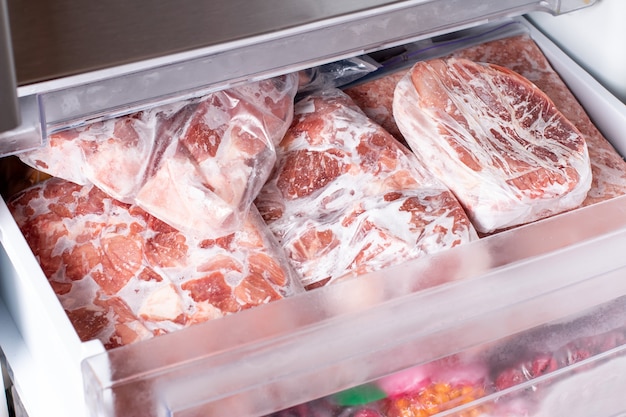 写真 冷蔵庫の冷凍庫の背景の肉。冷凍コンパートメントのクローズアップ豚肉、肉、鶏の脚。冷凍食品