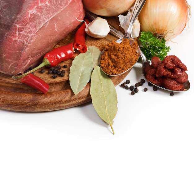 Meat and ingredients for goulash on chopping board, close-up, white background