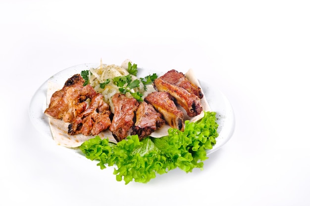 Meat kebab on ribs on lavash with onions and cabbage on a white plate, on an isolated white background