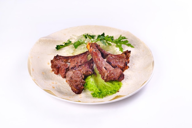 Meat kebab on ribs on lavash with onions and cabbage on a white plate, on an isolated white background.