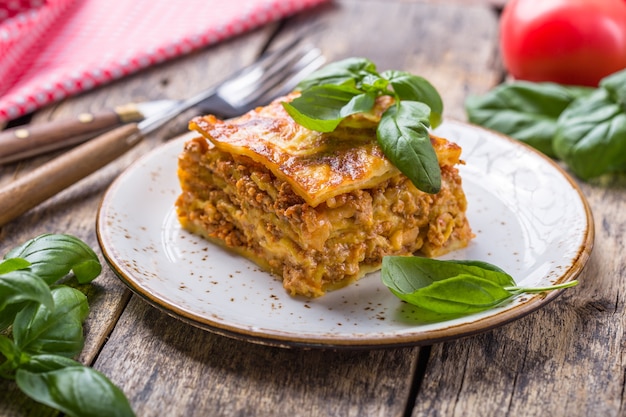 Meat lasagna with fresh basil and parmesan cheese in a plate on wooden table.