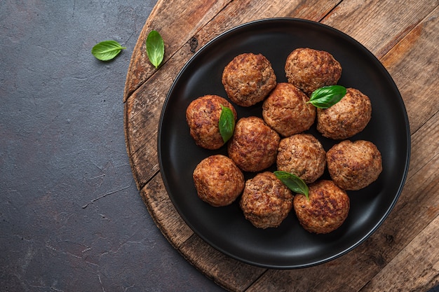 Meat meatballs in a black plate on a wooden board. Top view, copy space.