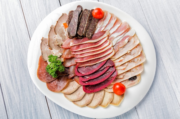 Meat plate with delicious pieces of sliced ham, cherry tomatoes, herbs and meat