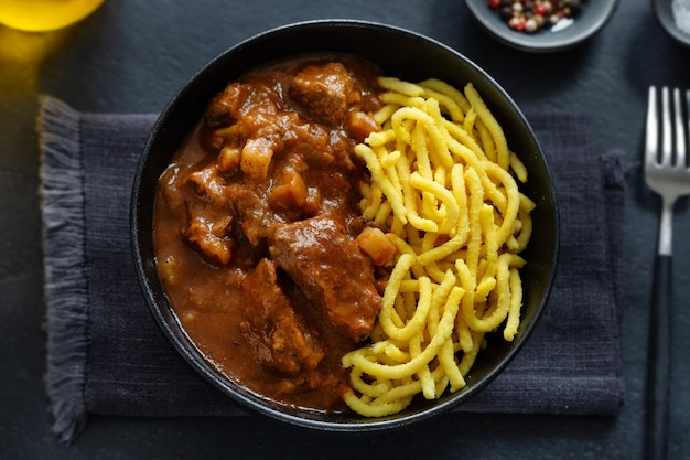 Meat ragout with noodles served in bowl on dark background. Closeup.